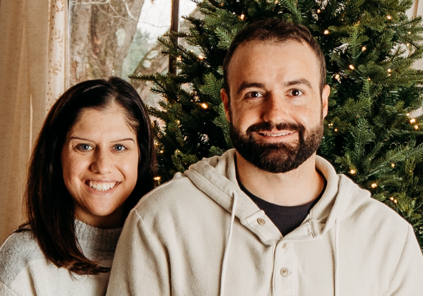 Brunette smiling woman and bearded smiling man in front of evergreen tree