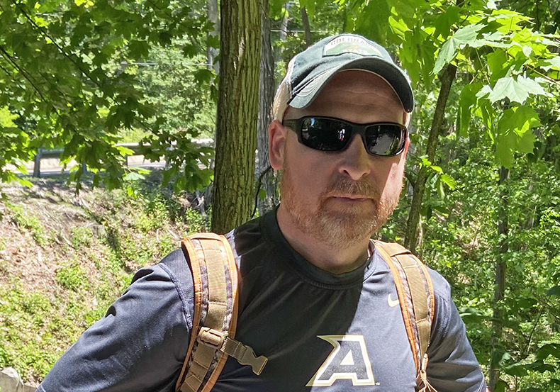 Bearded man wearing sunglasses and hat in the woods on a sunny day