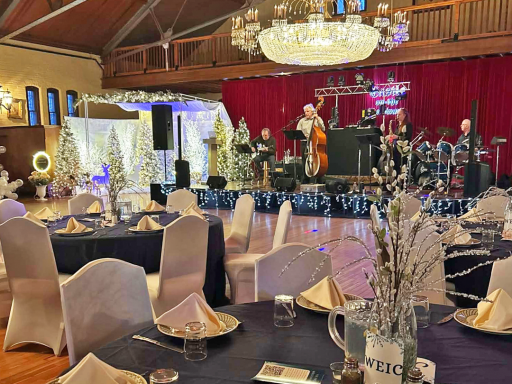 Tables set with fancy centerpieces as the band can be seen onstage in the background
